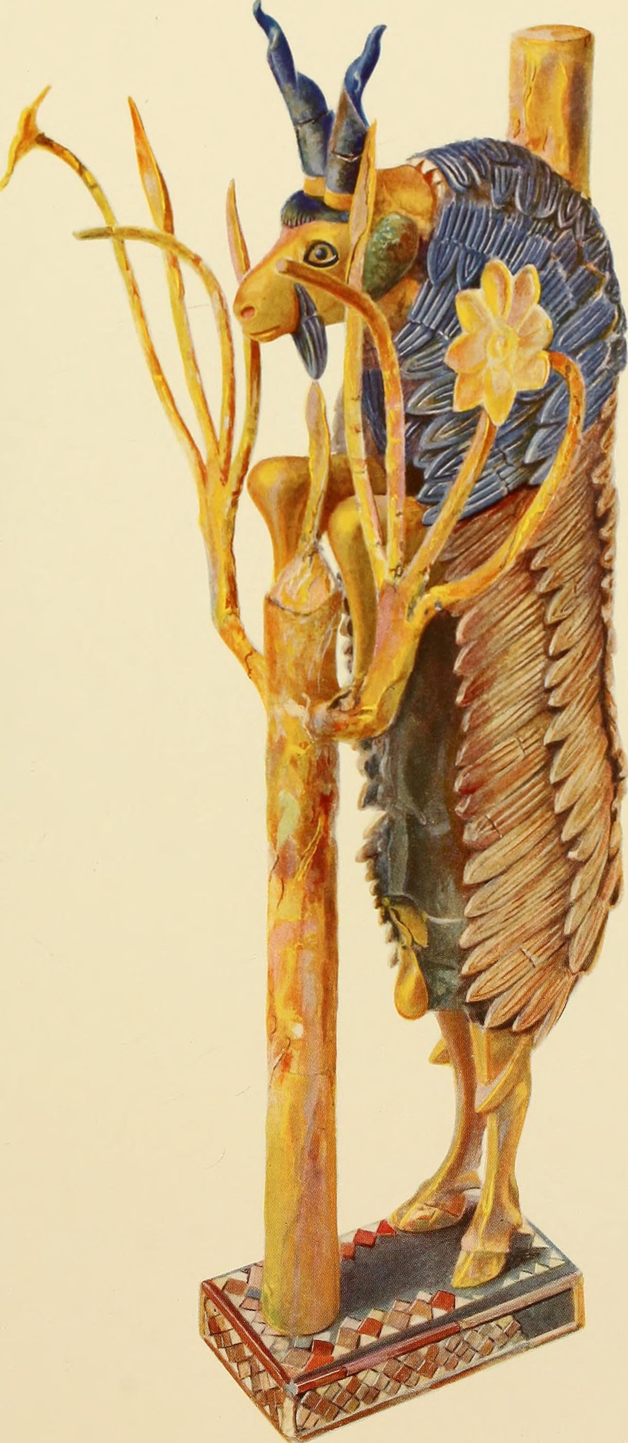 A goat standing upright on its hind legs, forelegs resting against a stylised flowering plant. The figure is covered in gold foil, with details in blue lapis lazuli and white shell, mounted on a rectangular base.