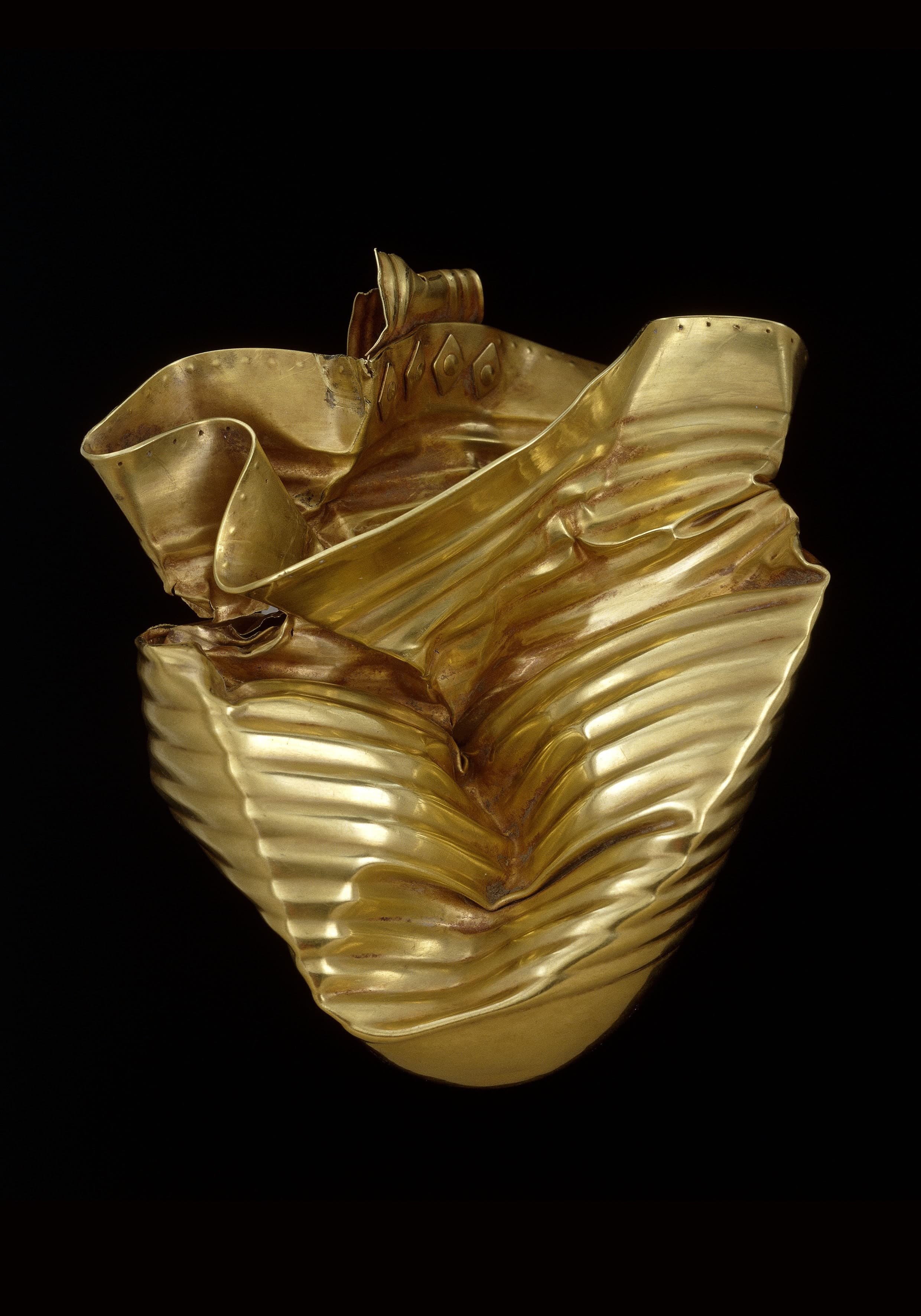 A small prehistoric gold cup with a rounded base and a single handle, shown as a thin-walled beaten vessel whose curved underside prevents it from standing upright alone.