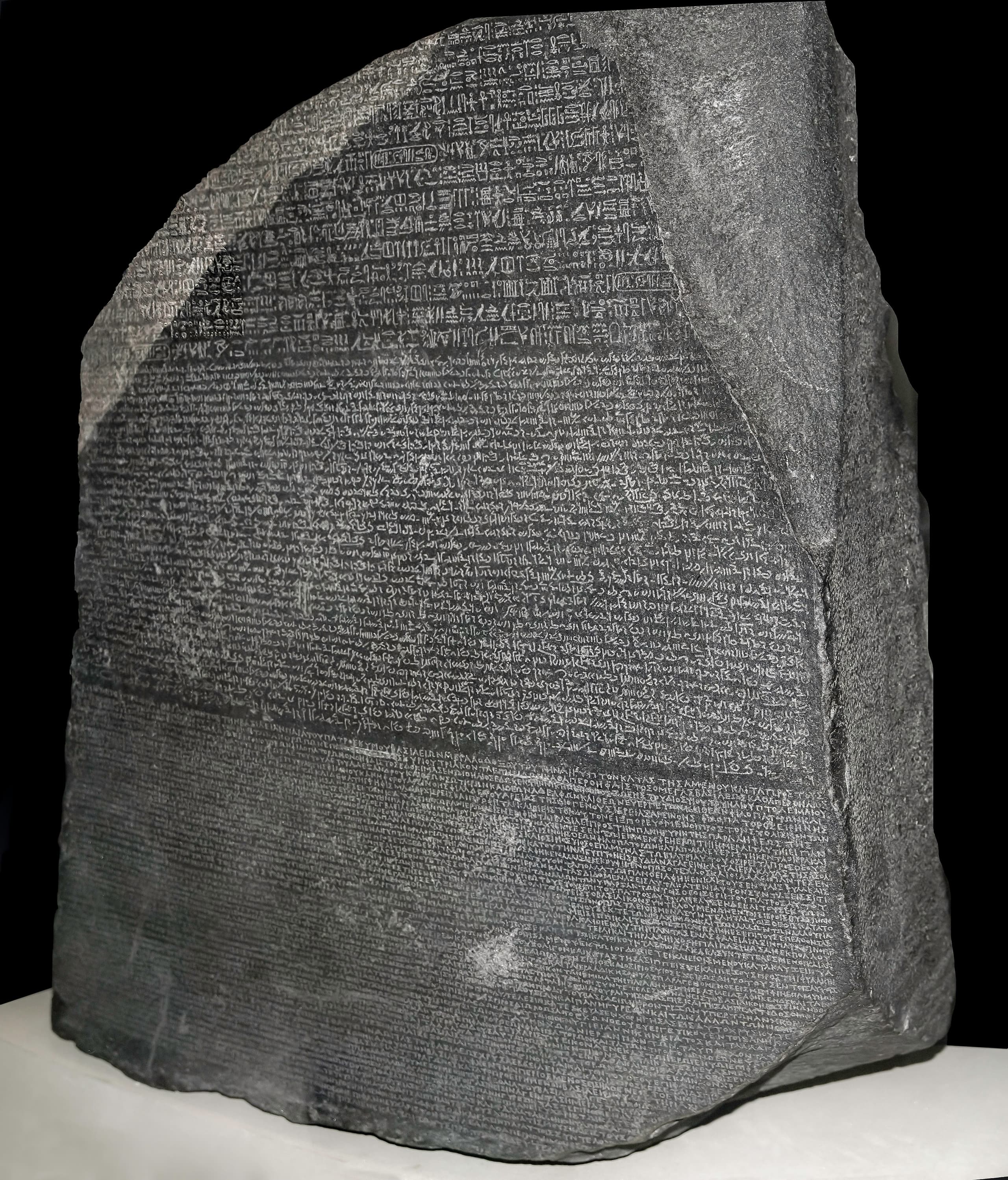 A dark grey granodiorite slab, broken at the top left and along the right edge, densely incised with three horizontal bands of text: sparse hieroglyphs at the top, close-packed cursive Demotic in the middle, and Greek lettering across the lower half. A pale pink vein runs through the upper left.