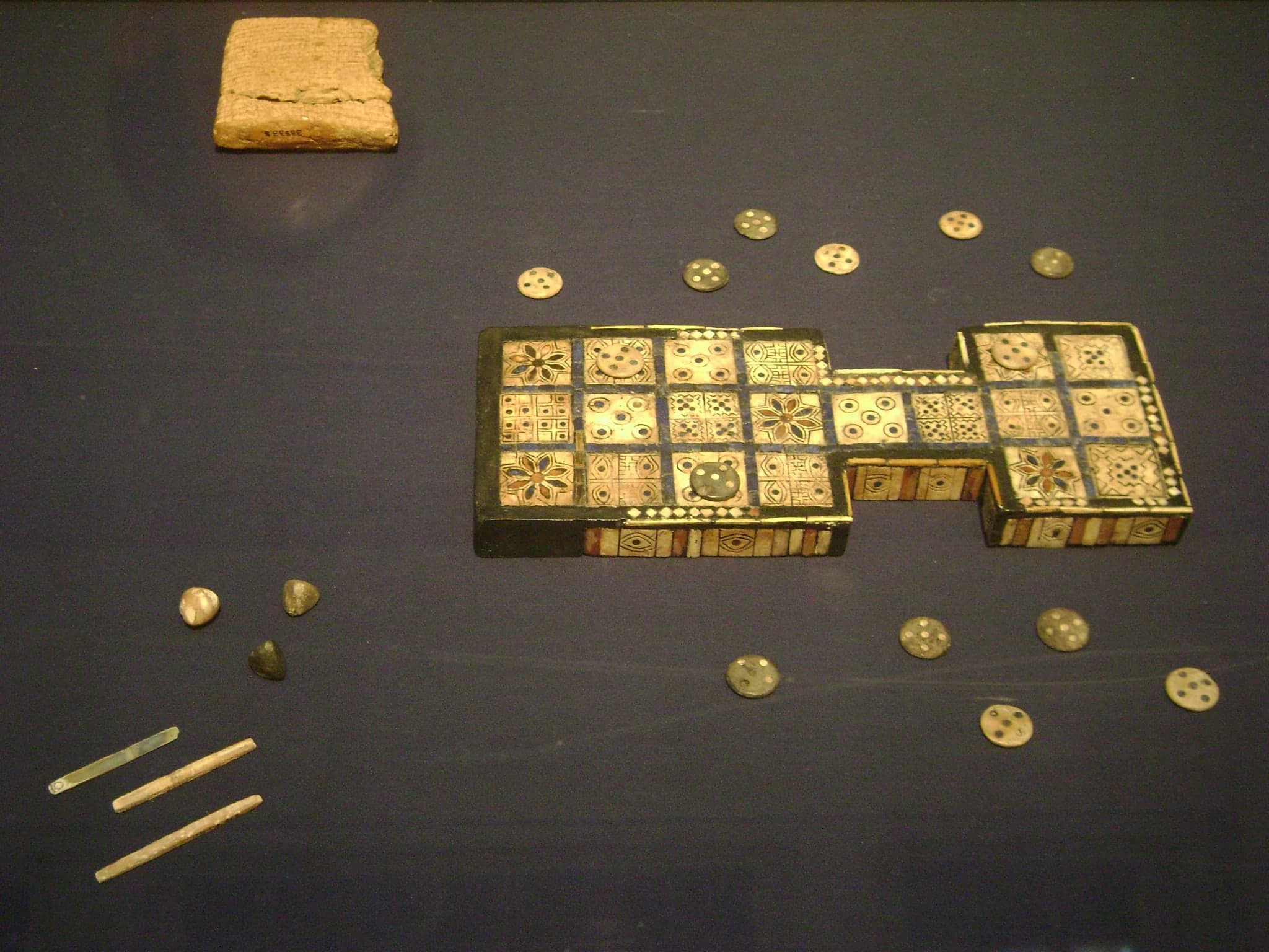 A rectangular wooden game board inlaid with shell and lapis lazuli, divided into twenty squares arranged in three sections: two blocks of six squares on each end and a narrow bridge of eight squares connecting them, with rosette patterns marking five of the squares.