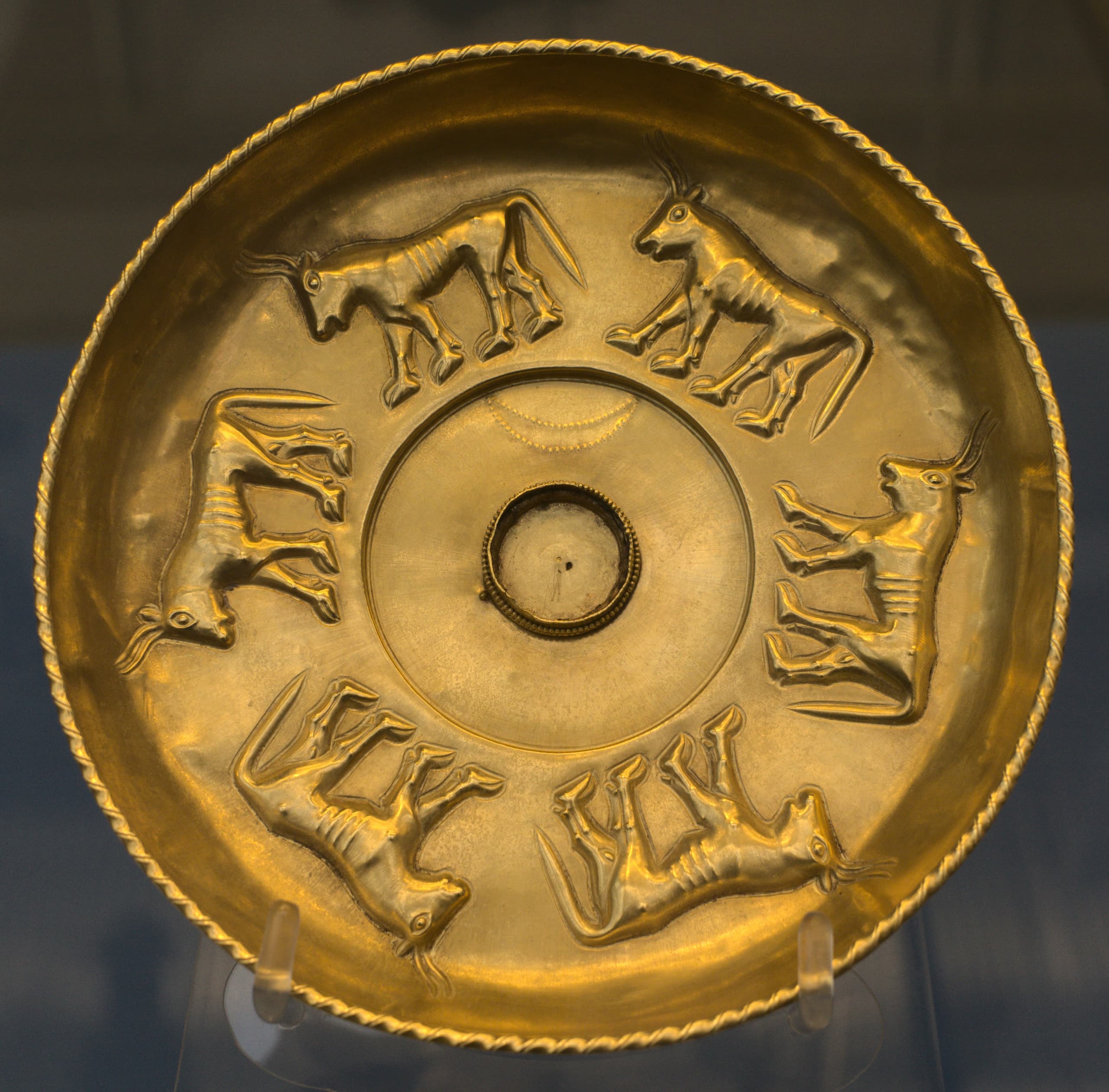 A shallow circular gold bowl of modest hand-held size, forming a simple phiale profile, shown as a museum object against a plain background.