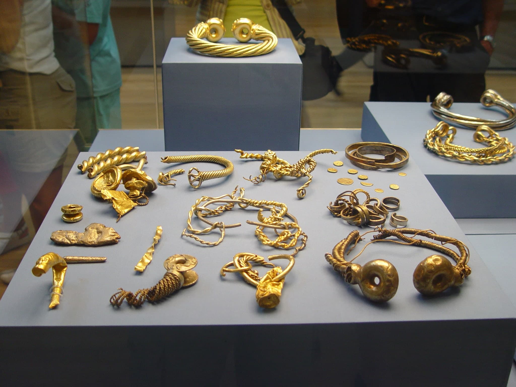 A heavy gold torc with a rope-twist body made of multiple strands wound together, ending in ornate cast terminals with ring-and-clasp fittings.
