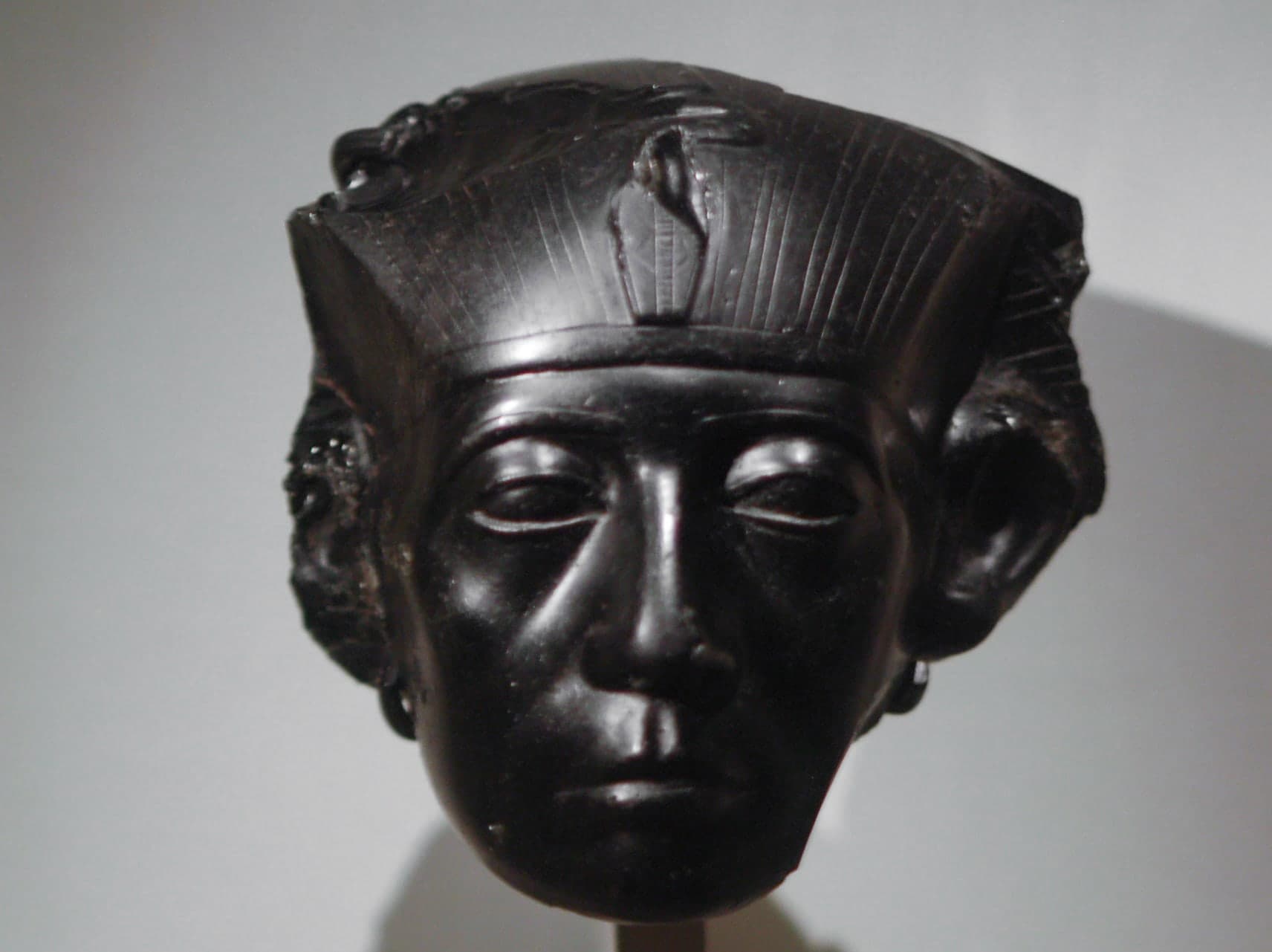 A carved stone head of a man with heavy, hooded eyes, a lined forehead, and a broad, unsmiling mouth. The face shows age and weariness rather than idealised youth.