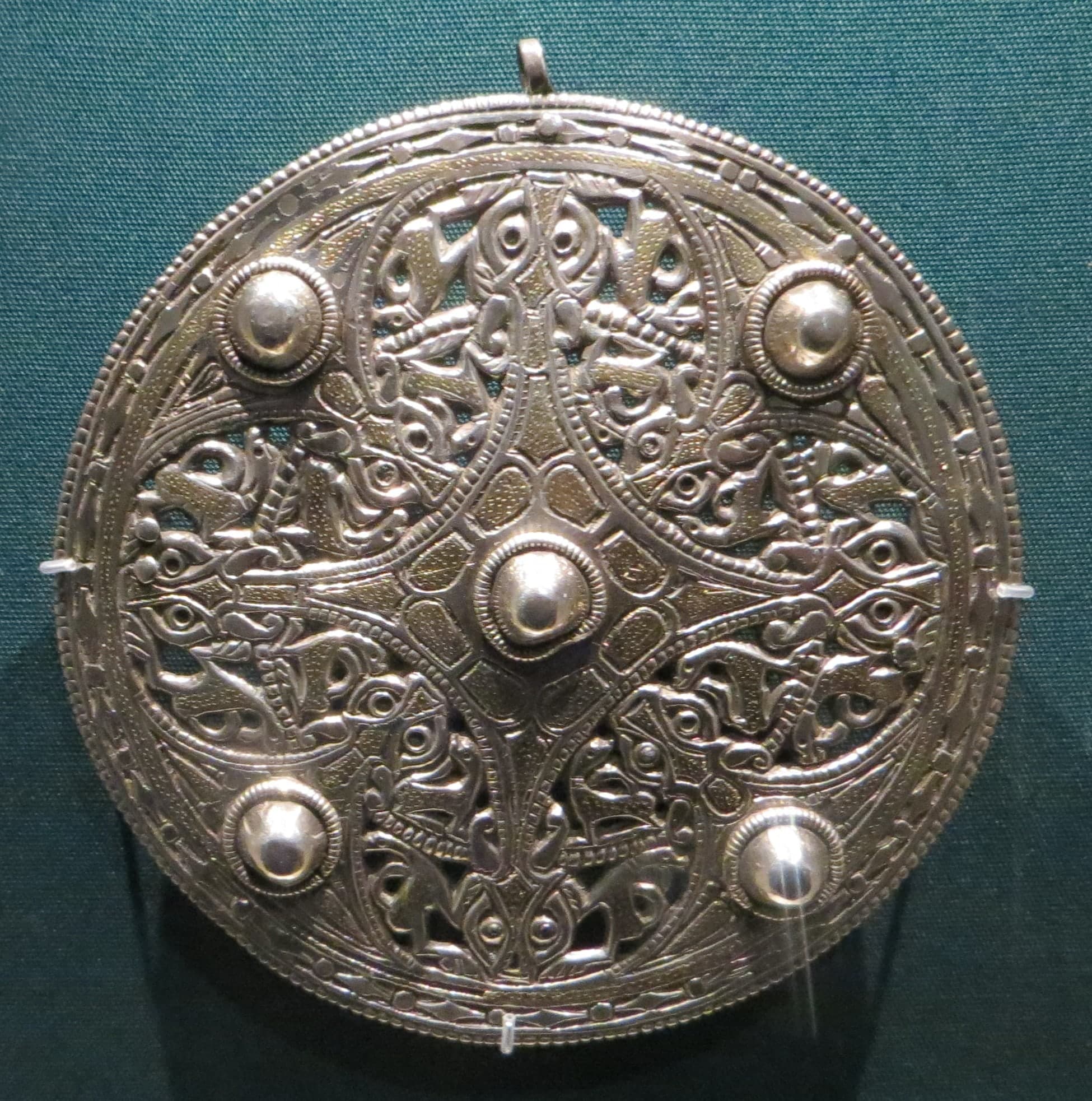 A circular silver disc brooch whose design is picked out in dark niello against the lighter metal.