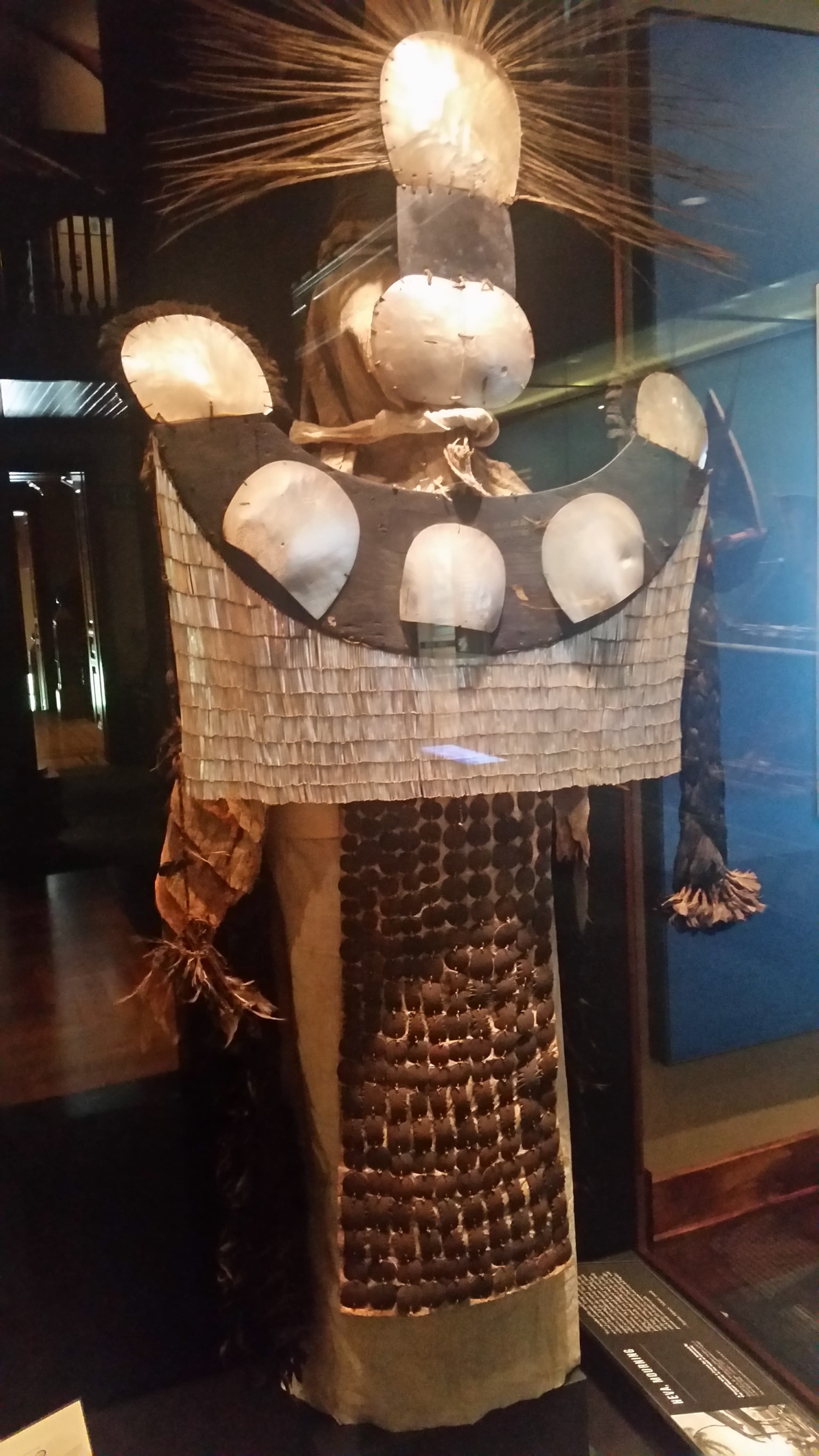 A ceremonial costume assembled from pearl shell breastplate, feather cape, and barkcloth elements, with coconut fibre cordage visible throughout the construction.