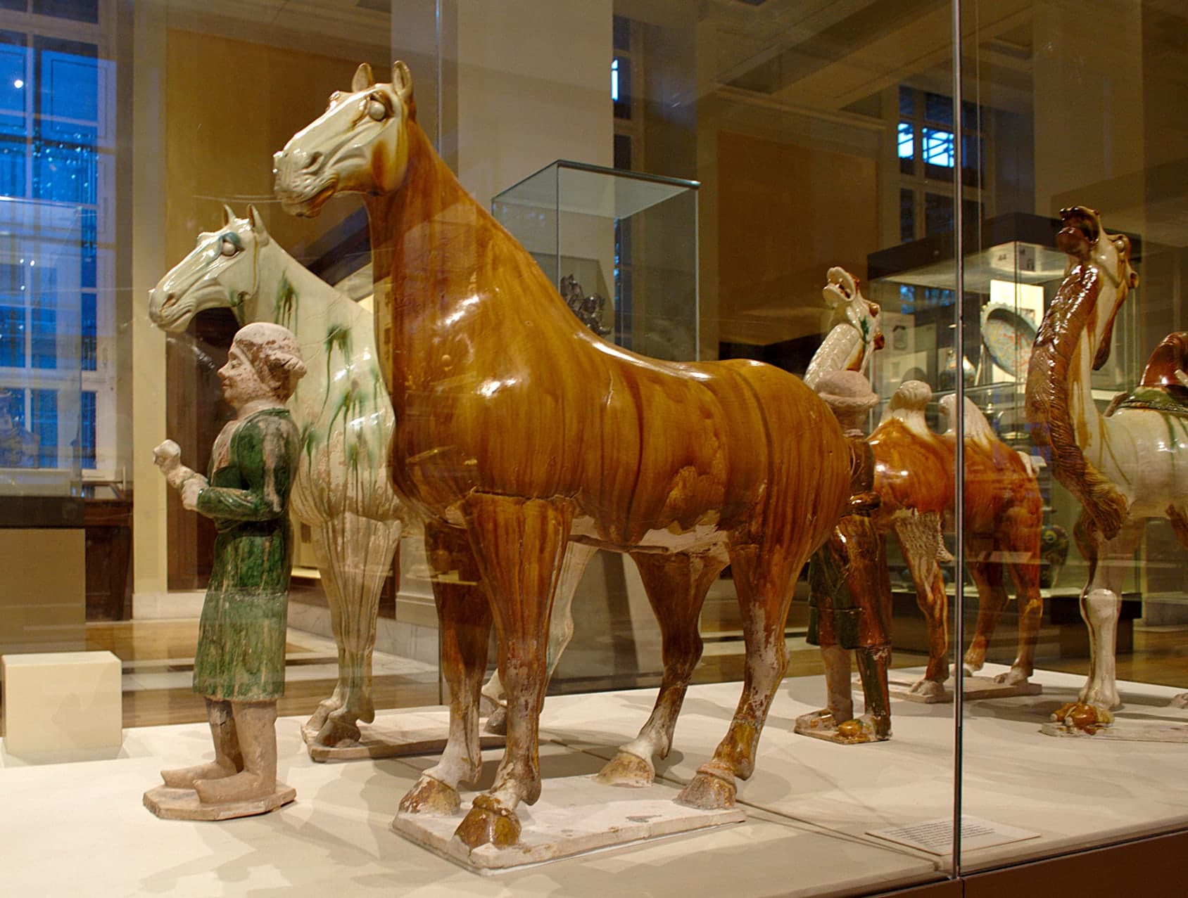 A group of earthenware figures of differing heights, arranged together against a plain pale background, their fired-clay surfaces mottled and dulled with age.