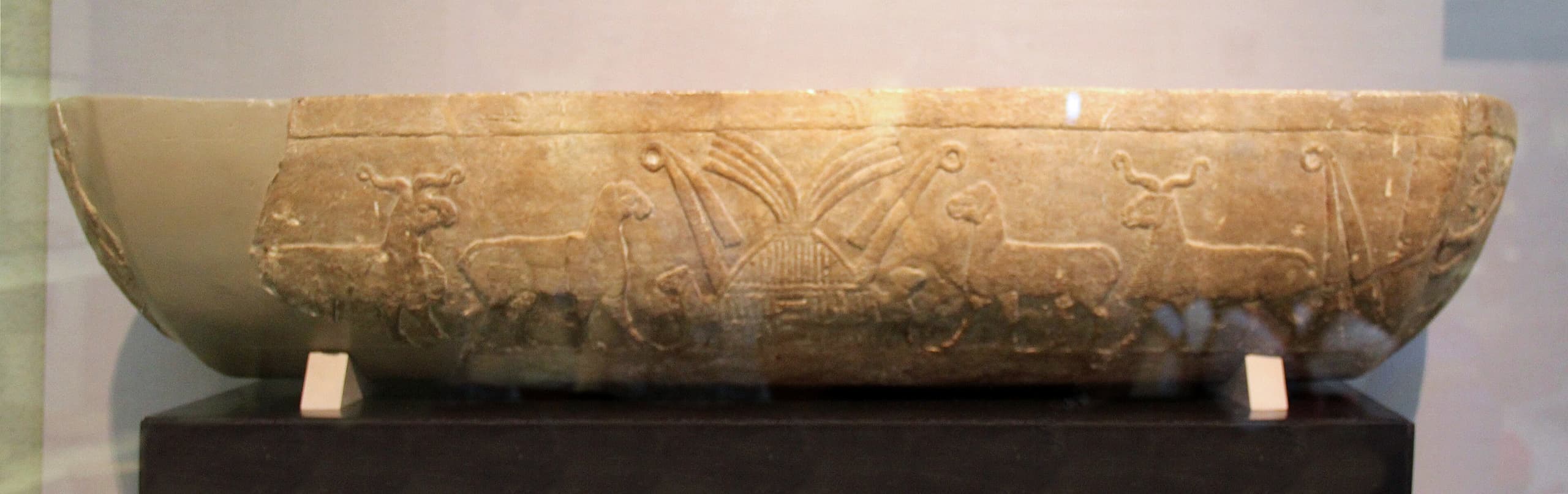 A small pale limestone trough with low relief carving of sheep walking in a line along the side, compact enough that its height is only about fifteen centimetres.