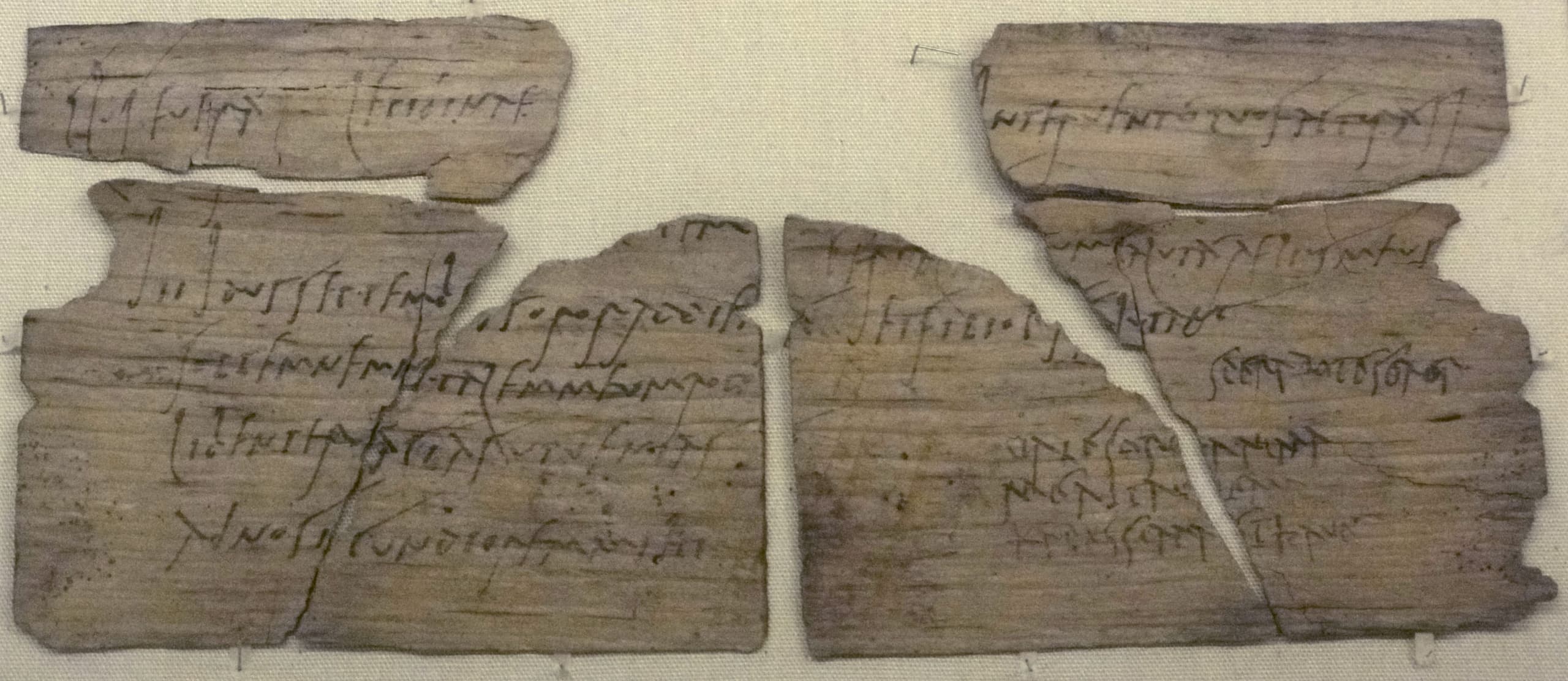 A close view of a thin wooden writing tablet, its surface marked with faint lines of handwritten ink text.