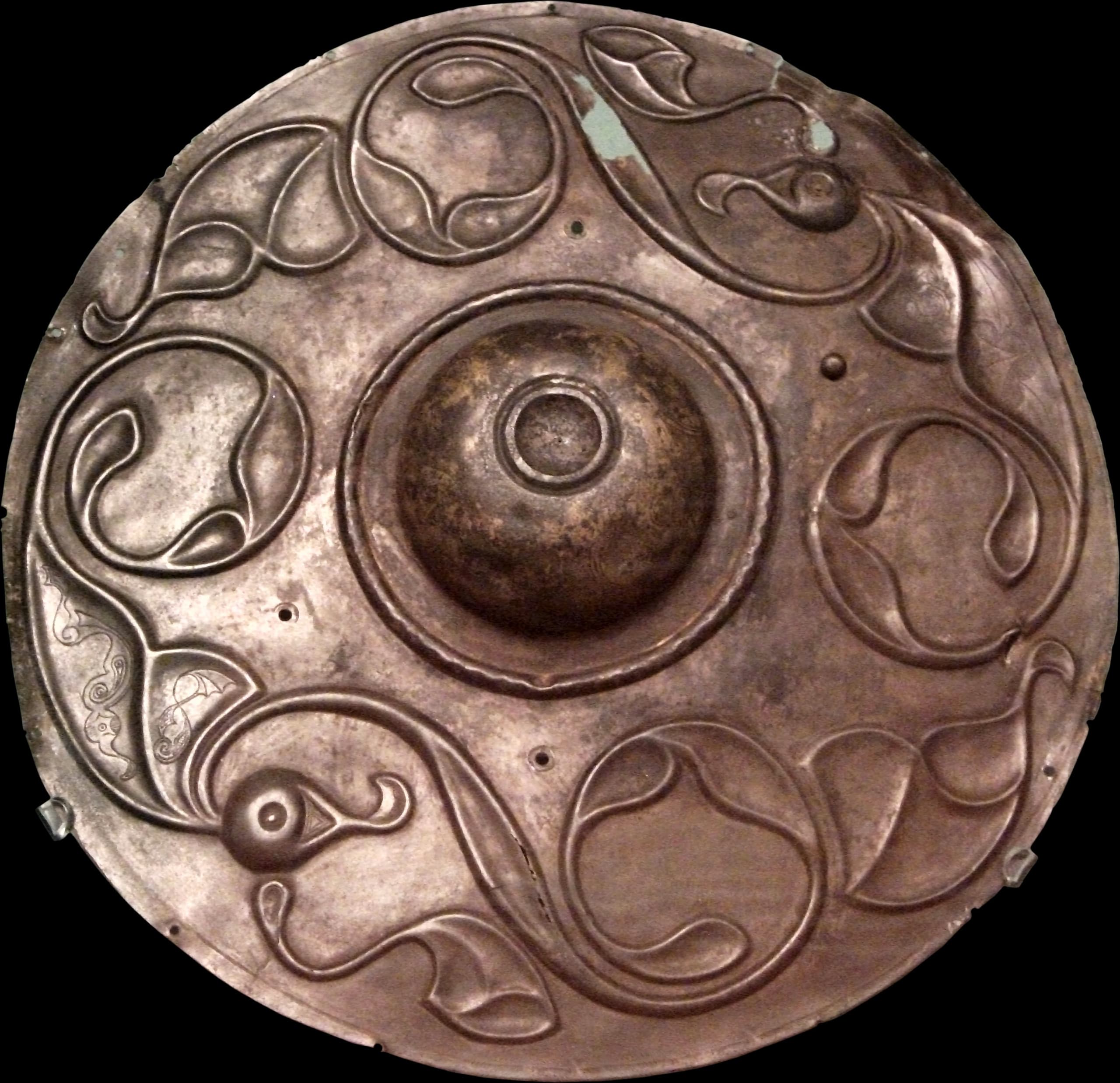A circular bronze disc with a central dome. Its surface is covered with the raised, flowing forms of two stylised birds, their wings outstretched to the edges and long, curled tail feathers sweeping around the lower curve.