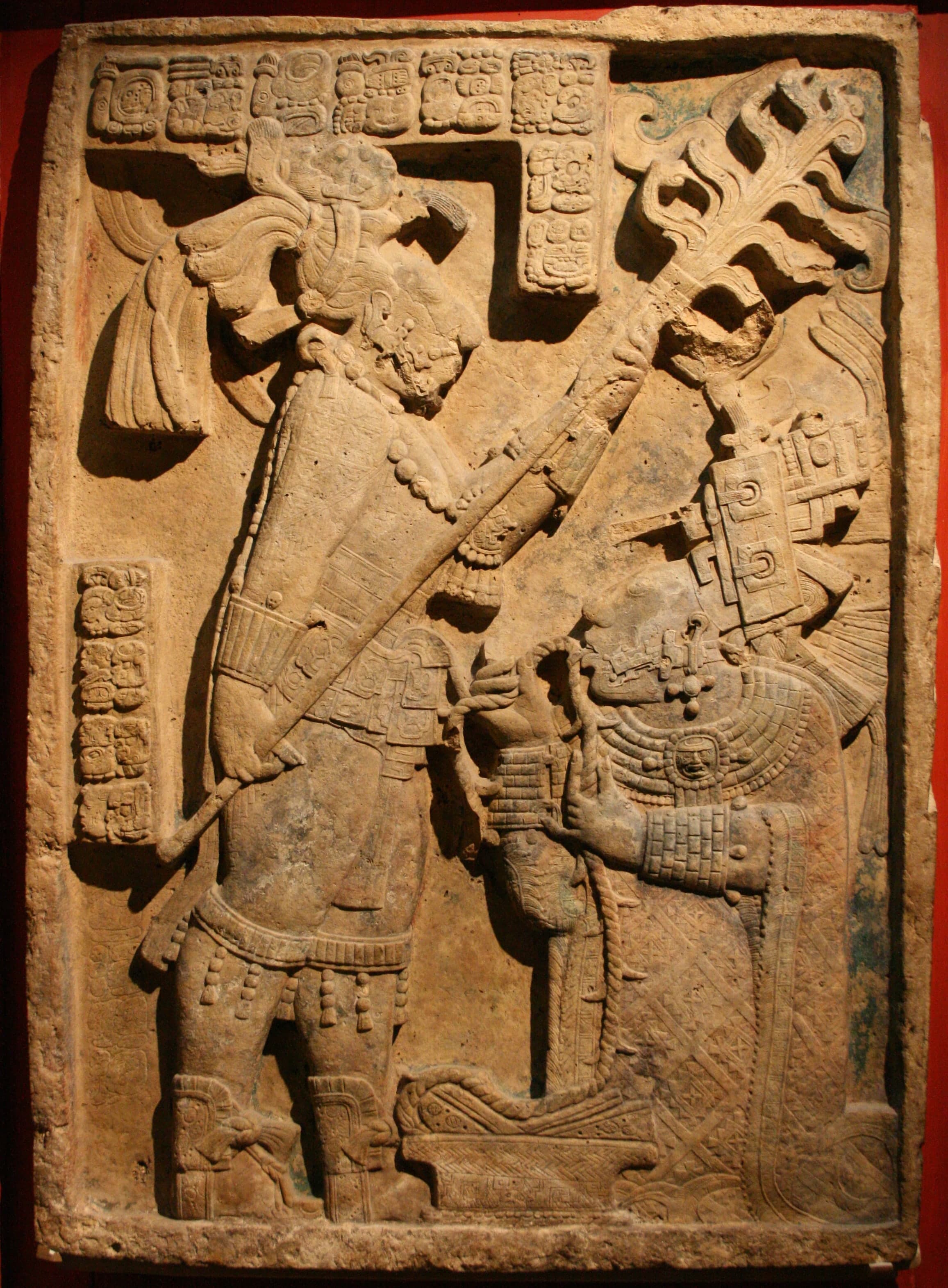 A limestone relief carved in mid-relief showing two figures: a kneeling woman on the right drawing a thorned rope through her tongue, and a standing man on the left holding a flaming torch above her. The surface is covered with Maya glyphs.