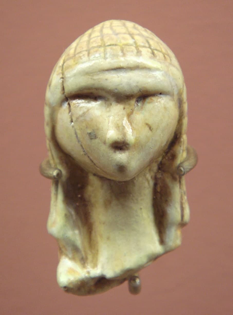 Tiny ivory head in three-quarter view: smooth face with clear brow and nose, a patterned hood or hair above, and a rough broken edge at the neck.